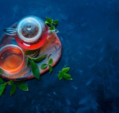 Teapot and double wall glass with tea leaves on a wooden coaster. Dark blue background flat lay with copy space.