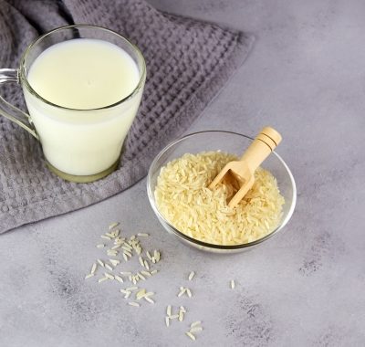 Rice milk in a glass mug and a rice grains in a bowl on a grey background.