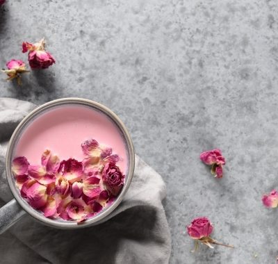 Rose moon milk in grey cup and rose petals on grey. Top view.