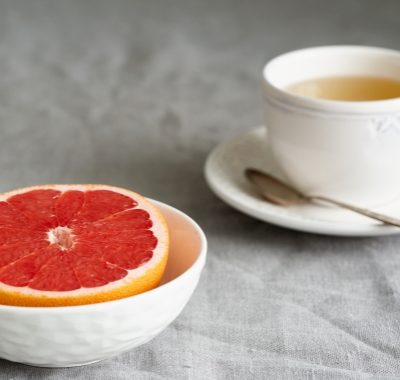 Still life with half of grapefruit in bowl and cup of herb tea on table