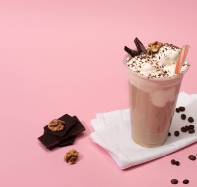 High angle view of disposable cup of milkshake with walnuts, chocolate pieces and coffee grains on