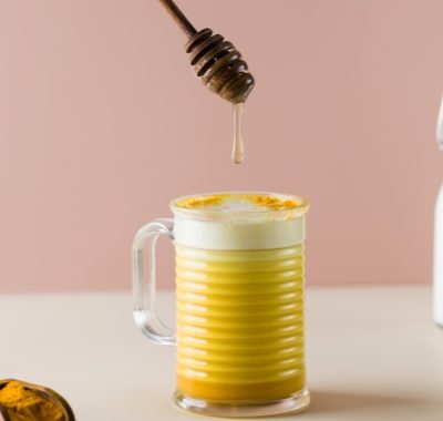 A drop of honey drips into a latte turmeric mug. Moon milk for better sleep.